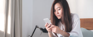 Woman looking at her phone in a bedroom indicating that she got an alert.