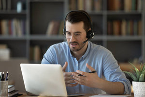 Remote consulant with headset talking to client through video chat with a pen in his hand.