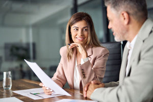 Consultant smiling at client and holding a piece of paper in a suit with a pen in hand.