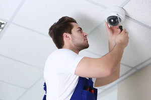 Man installing dome security camera with a screwdriver in a white shirt and overalls.