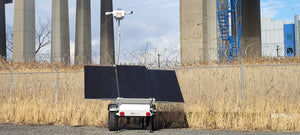 Vorp energy solar powered surveillance trailer for with pole mounted bullet cameras with razor wire in background.